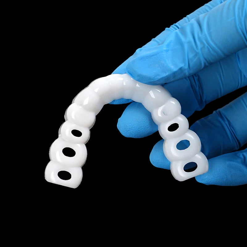 A hand wearing a blue glove holds a clear cosmetic denture teeth kit, shaped like an arc.