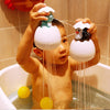 A young child is playing with white bath toys shaped like a duck and a penguin that spray water into the tub.