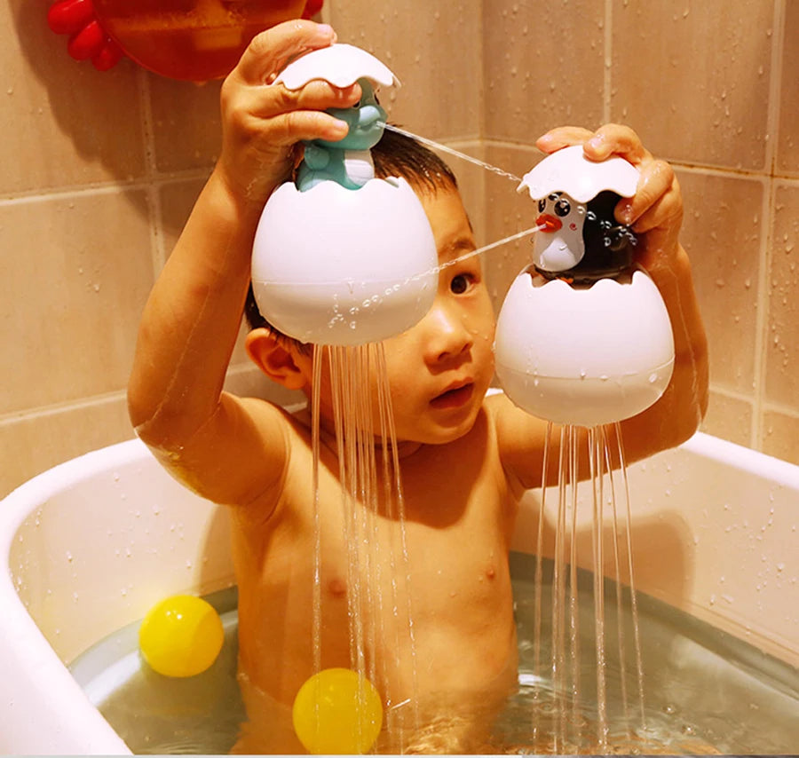 A young child is playing with white bath toys shaped like a duck and a penguin that spray water into the tub.