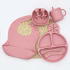 A pink silicone baby tableware set including a bib, suction plate, and small cup.