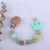 A beaded pacifier clip made of beech wood and silicone beads with a light green crown charm on a white background.