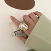 A hand wearing a gold starfish pearl ring, resting on a light green fabric and next to a small box.