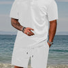 A man wearing a white jacquard short-sleeve shirt and matching drawstring shorts outdoors near the water.
