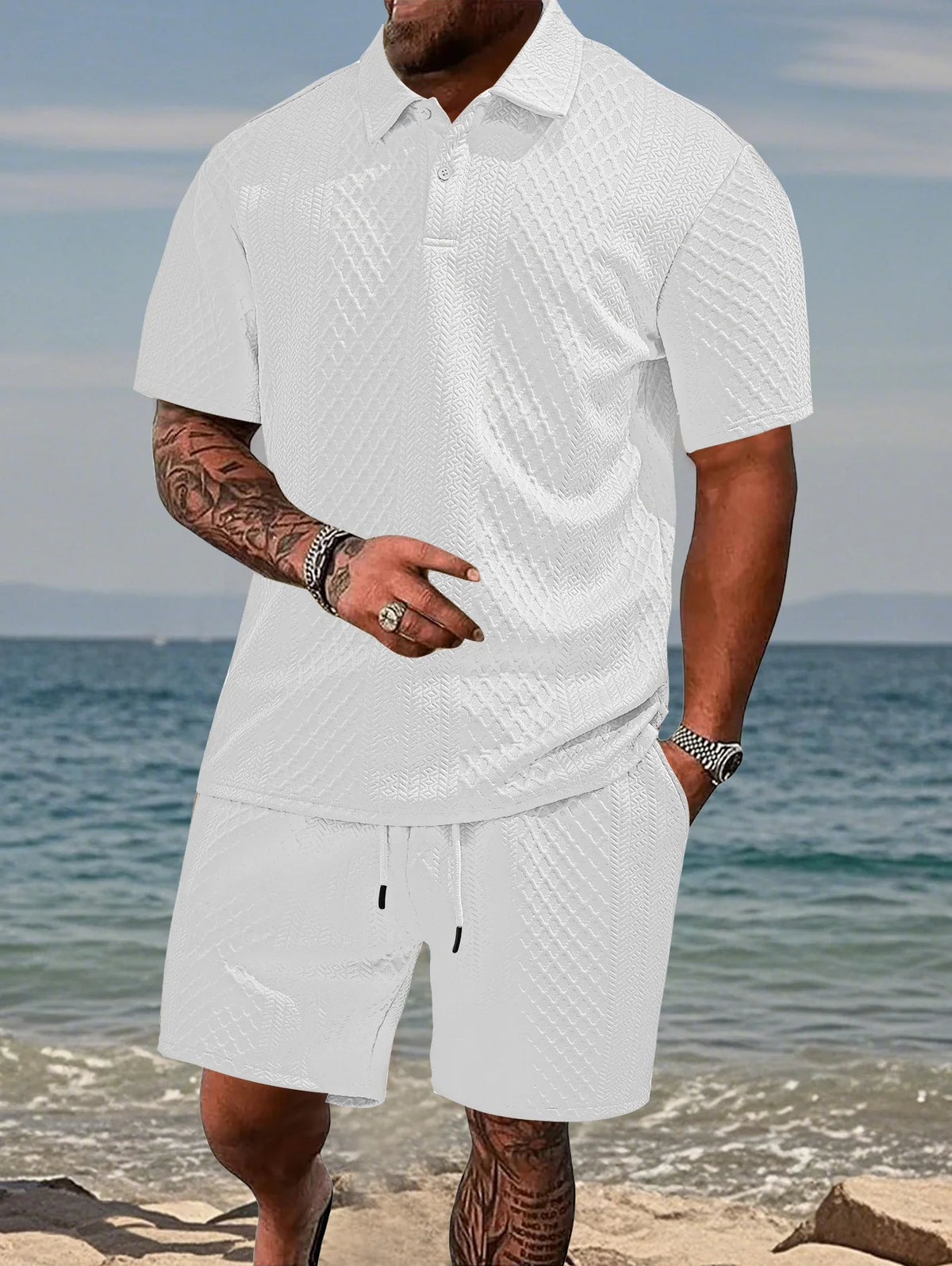 A man wearing a white jacquard short-sleeve shirt and matching drawstring shorts outdoors near the water.