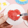A hand applies red paint to a heart shape on white puffy texture painting paper for kids.