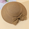 A beige straw sun hat with a wide brim and a matching bow, resting on a light background.
