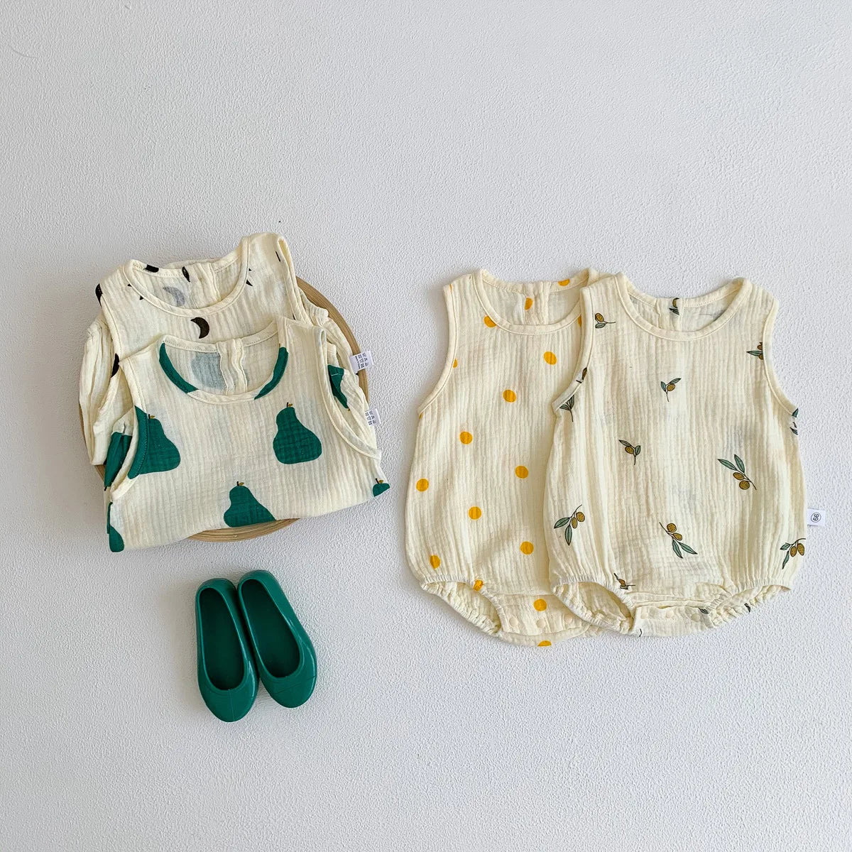 A set of cream-colored baby cotton sleeveless jumpsuits or bodysuits with green and yellow floral patterns.
