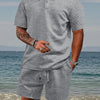 A man wearing a gray jacquard short-sleeve shirt and matching drawstring shorts standing near the ocean.