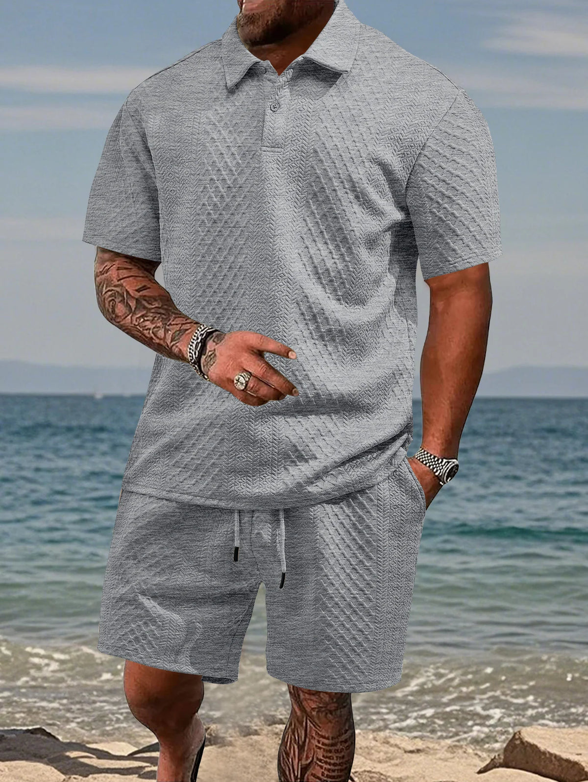 A man wearing a gray jacquard short-sleeve shirt and matching drawstring shorts standing near the ocean.