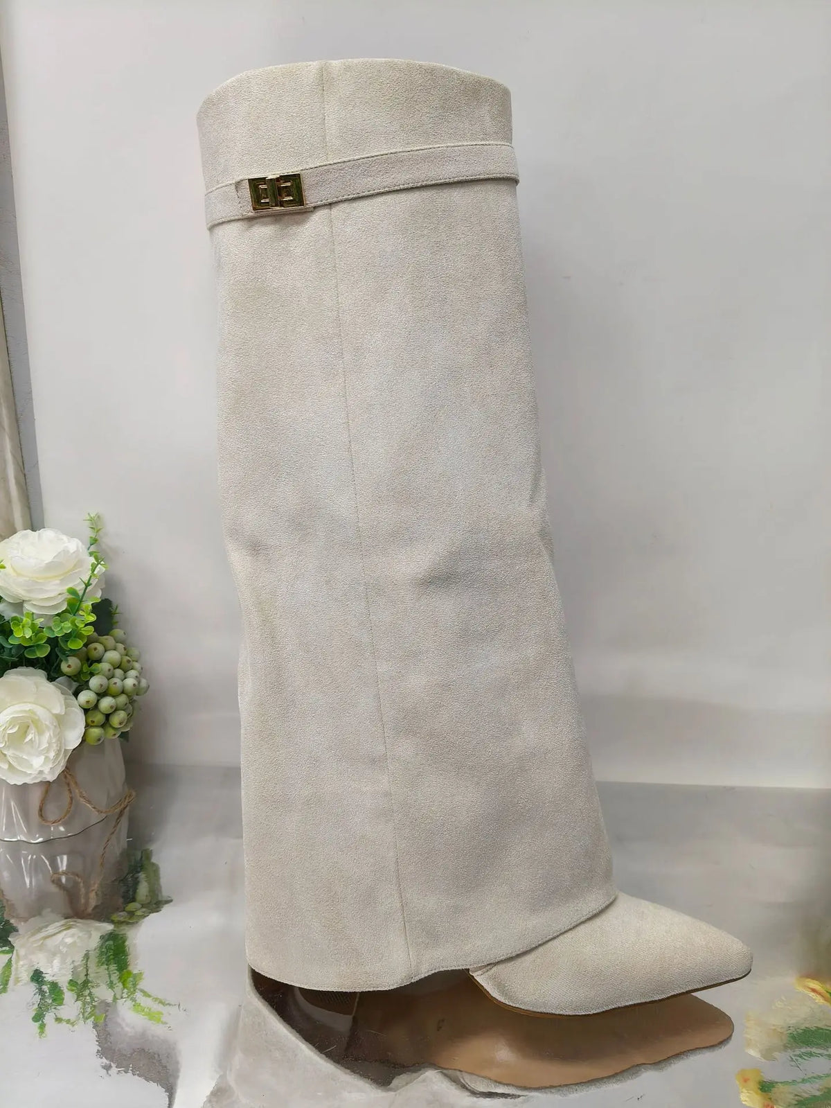 A beige knee-high boot with a chunky heel and a gold metal buckle.
