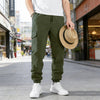 A man wearing olive green casual cargo pants and white sneakers stands on a city street.