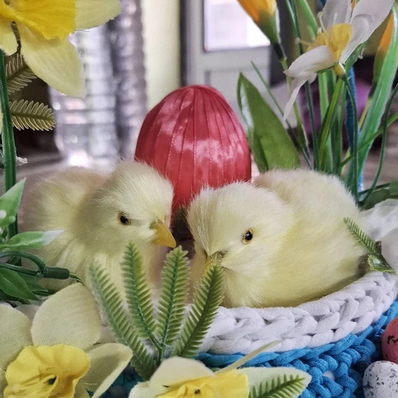 Myk gul plysjkyllingdekorasjon omgitt av grønne blader og gule blomster.