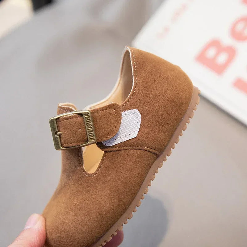 A close-up of a tan retro non-slip kids' moccasin shoe with a brass hook-and-loop closure.
