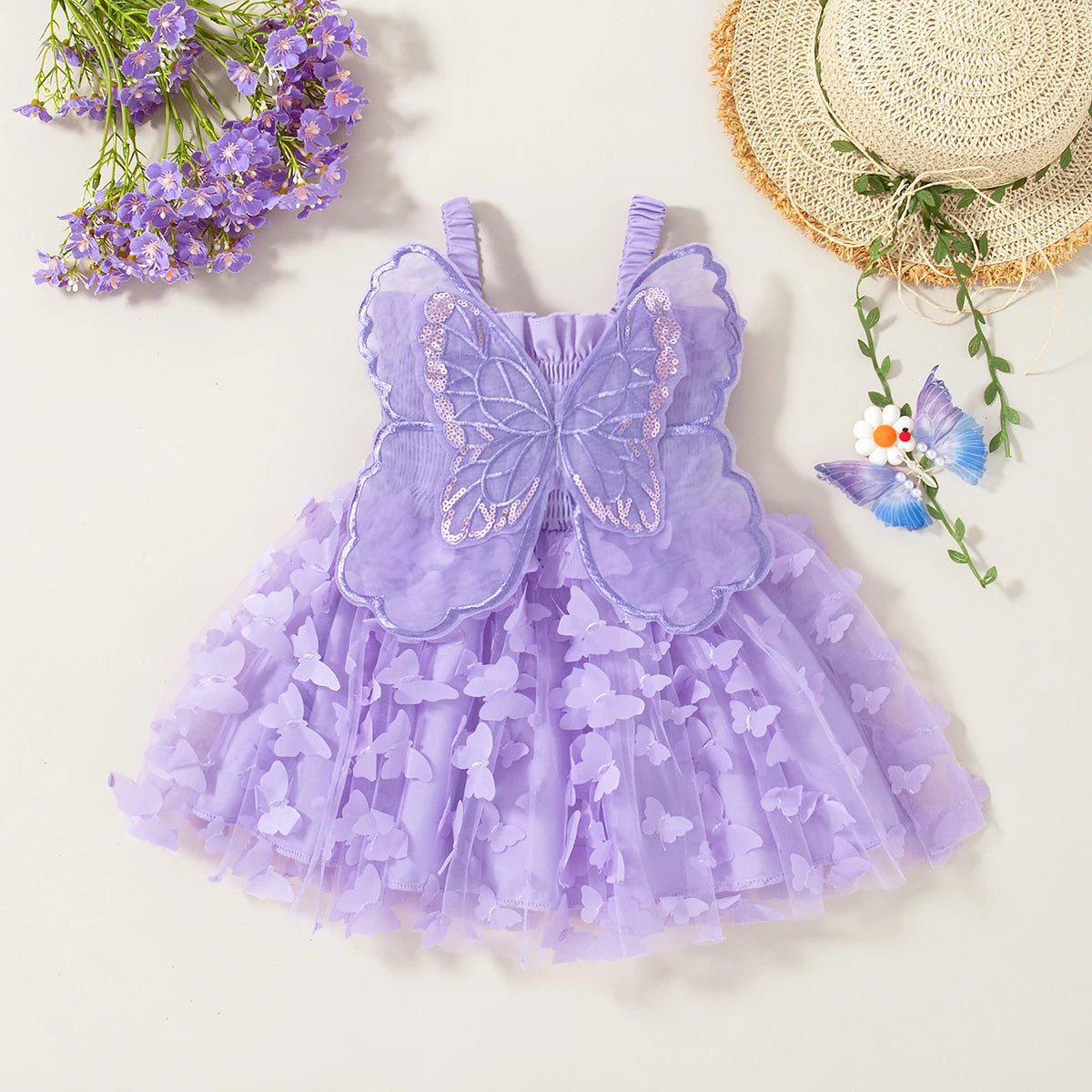 A purple tulle butterfly dress for a baby girl displayed on a light background with lavender flowers and a straw hat.