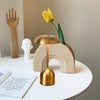 A minimalist gold and white table lamp with a yellow tulip decoration sits on a white surface.