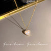 A gold chain necklace with a heart-shaped pendant featuring a clear crystal or stone, displayed on a light surface.