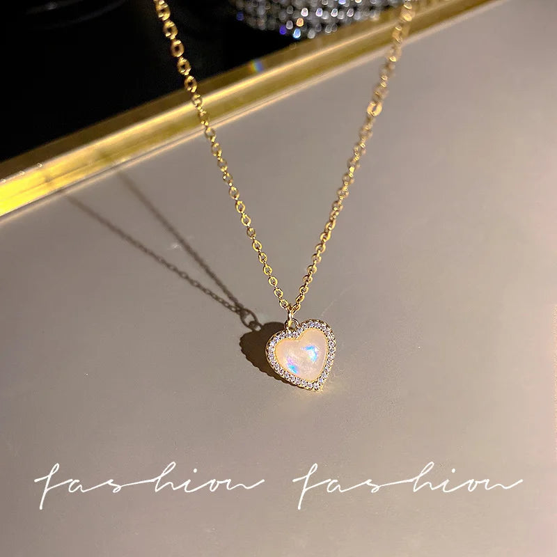 A gold chain necklace with a heart-shaped pendant featuring a clear crystal or stone, displayed on a light surface.