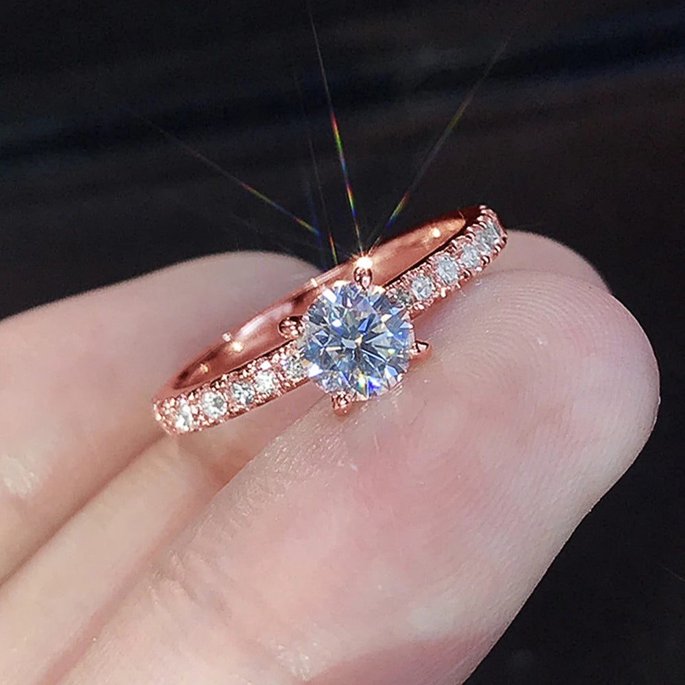 Nærbilde av en rosegull forlovelsesring med en rund kubisk zirkonia omgitt av små pavédiamanter.