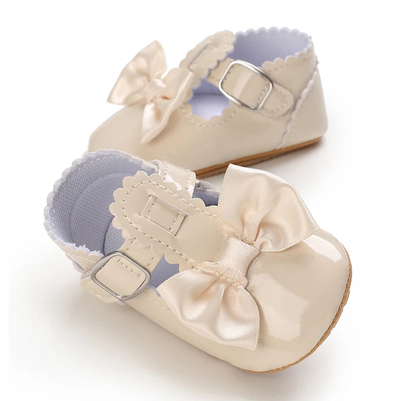 A pair of light beige baby first walker shoes with pink satin bows and soft leather soles.