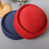 A red straw pillbox sun hat and a navy blue straw hat are displayed on a gray surface.