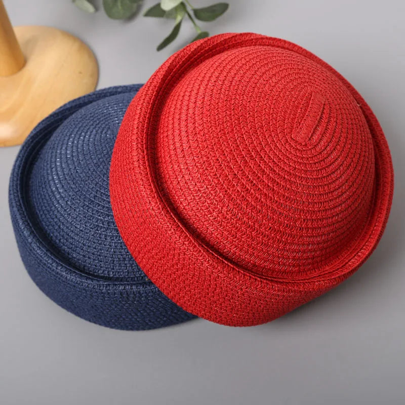 A red straw pillbox sun hat and a navy blue straw hat are displayed on a gray surface.