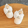 Pair of white lace baby first walker shoes with bows resting on a wooden surface.