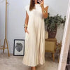A woman wearing a cream pleated midi dress with a round neckline standing indoors.
