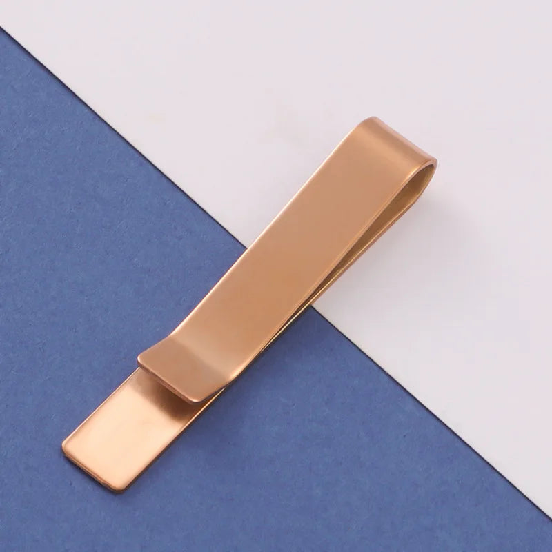 A rose gold metal tie clip lying diagonally on a blue-gray fabric background.