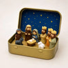 A miniature nativity scene featuring figures and an animal set inside a gold-colored metal box with a blue starry background.