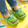 A pair of bright green kids shark clog sandals with anti-slip soles resting on a yellow surface.