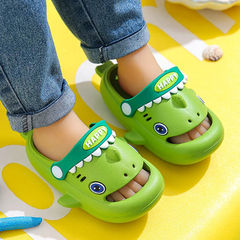 A pair of bright green kids shark clog sandals with anti-slip soles resting on a yellow surface.