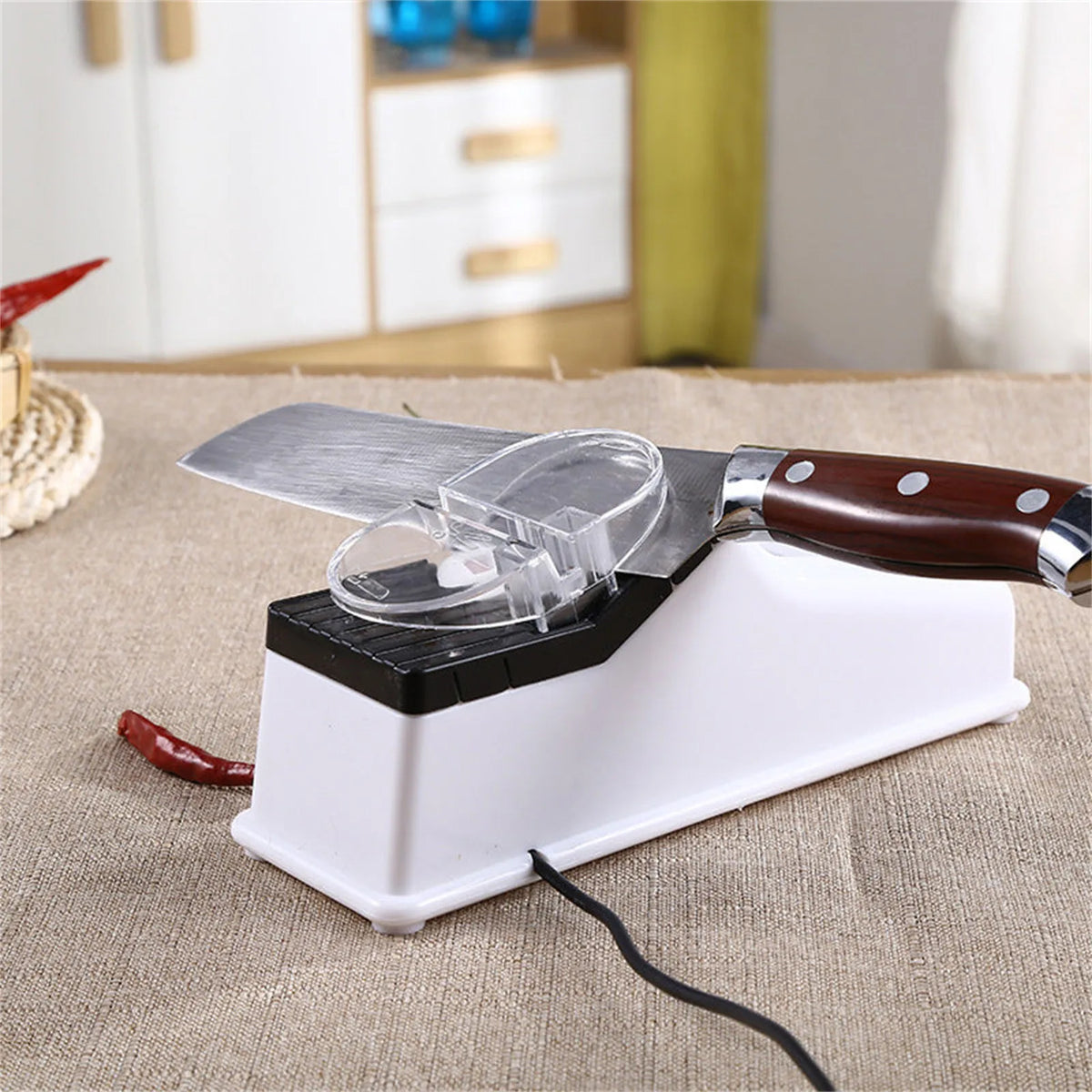 A white electric knife sharpener with a protective cover and a wooden handle is shown on a beige fabric surface.
