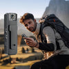 A man is holding a compact HD action camera with night vision features outdoors against a mountainous backdrop.