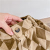 A hand is adjusting the pocket of khaki green plaid kids' washed cotton harem pants.