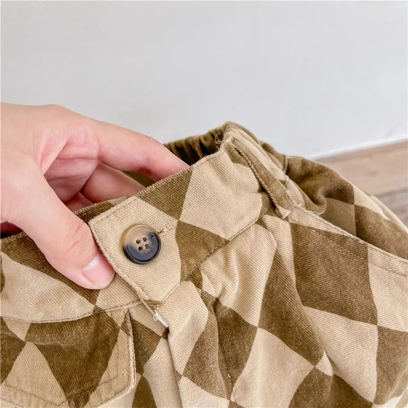 A hand is adjusting the pocket of khaki green plaid kids' washed cotton harem pants.