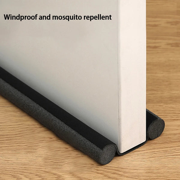 A white door bottom seal strip with a black flexible rubber seal is shown on a wooden surface.