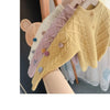 A display of knitted cardigan sweaters in various pastel colors, featuring pom-pom trims.