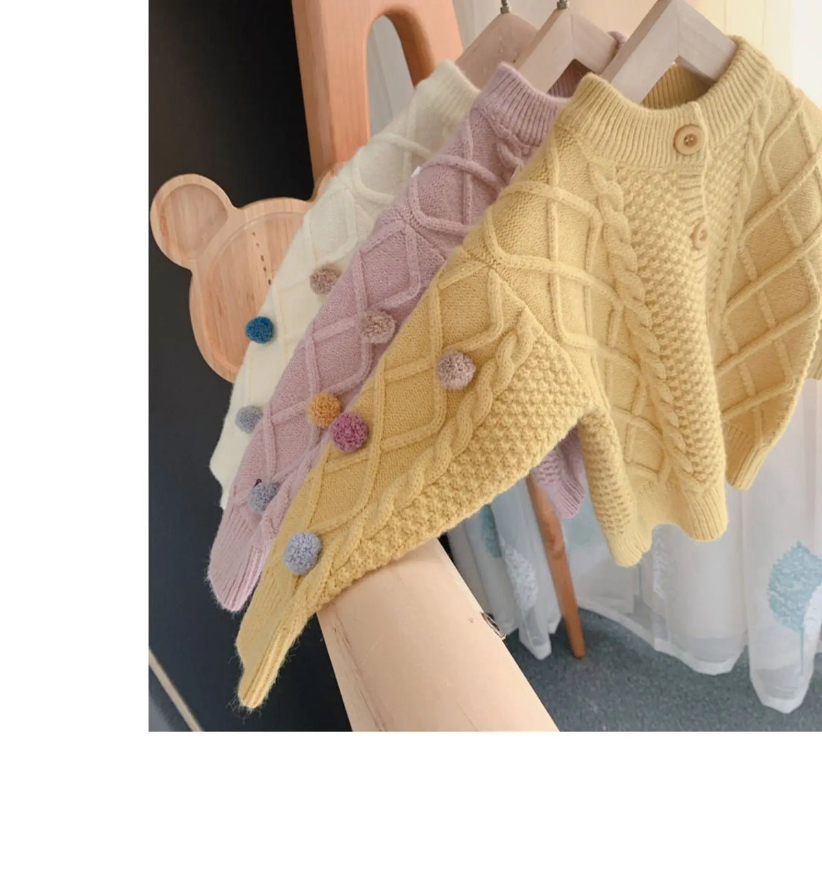 A display of knitted cardigan sweaters in various pastel colors, featuring pom-pom trims.