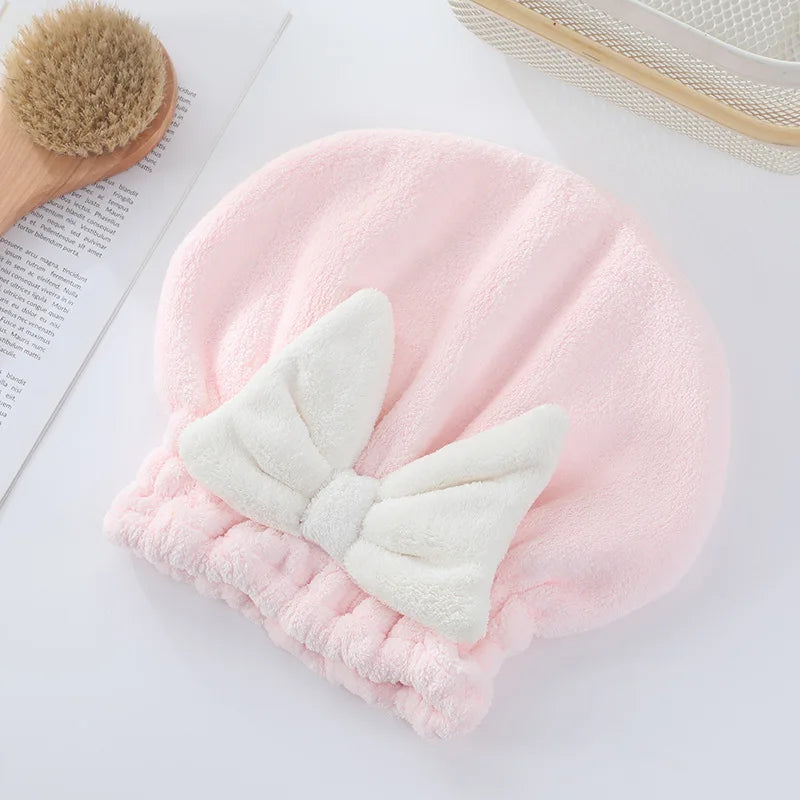 Gorro de microfibra rosa para secar el cabello con un lazo blanco sobre una superficie blanca.