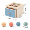 A wooden box with four circular openings for sorting, showing various colored balls and a coin drop toy.