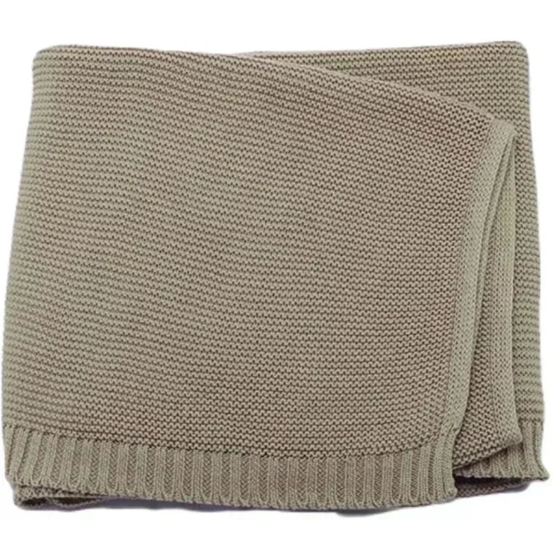 A folded beige knit baby blanket with a ribbed edge.
