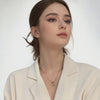 A woman wearing a cream blazer and a dainty gold heart pendant necklace with a snake chain.