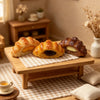 Et trebrett med tre gyldne croissanter på en rutet duk mot en myk bakgrunn.