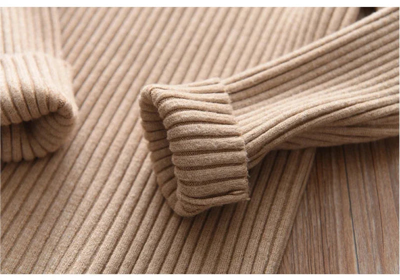 A close-up of a beige knit turtleneck sweater for kids, showing the ribbed texture and cuff detail.