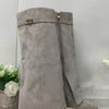 A pair of taupe suede knee-high boots with chunky heels and a gold metal buckle.