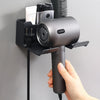 Una mano sostiene un soporte de pared para secador de pelo gris, mostrando su uso para varios secadores.