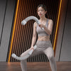 A woman wearing light gray athletic wear is demonstrating a workout with white cordless battle ropes against a textured wall.