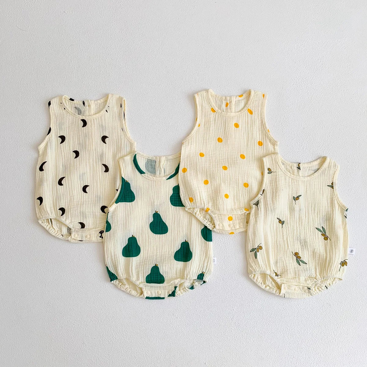 A set of three cream-colored baby cotton sleeveless bodysuits featuring small dark leaves and fruit patterns.