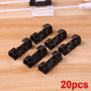 A collection of twenty black self-adhesive cable management clips laid out on a wooden surface.