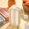 A clear plastic ice cube tray with a mold for a water bottle is shown next to a pineapple and other food items.